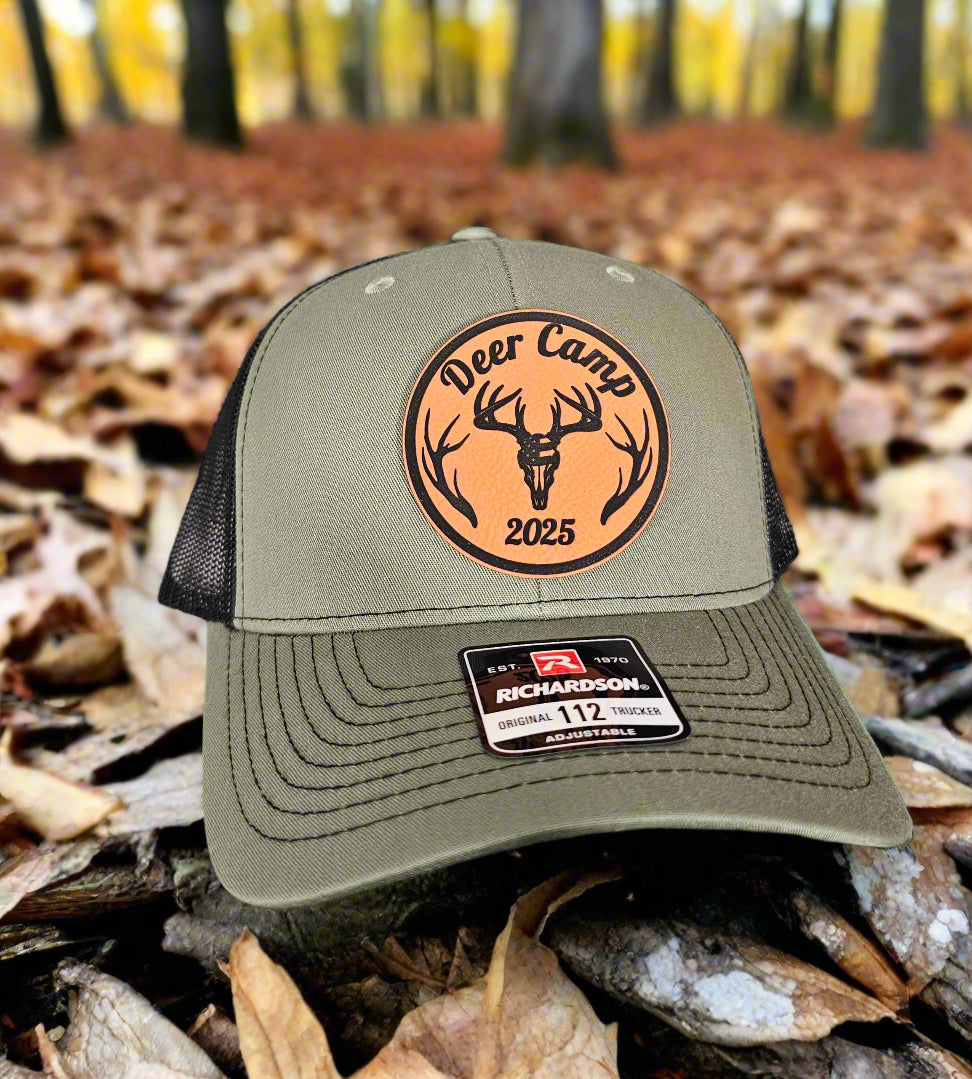Green cap with 'Deer Camp 2025' patch on a forest floor background